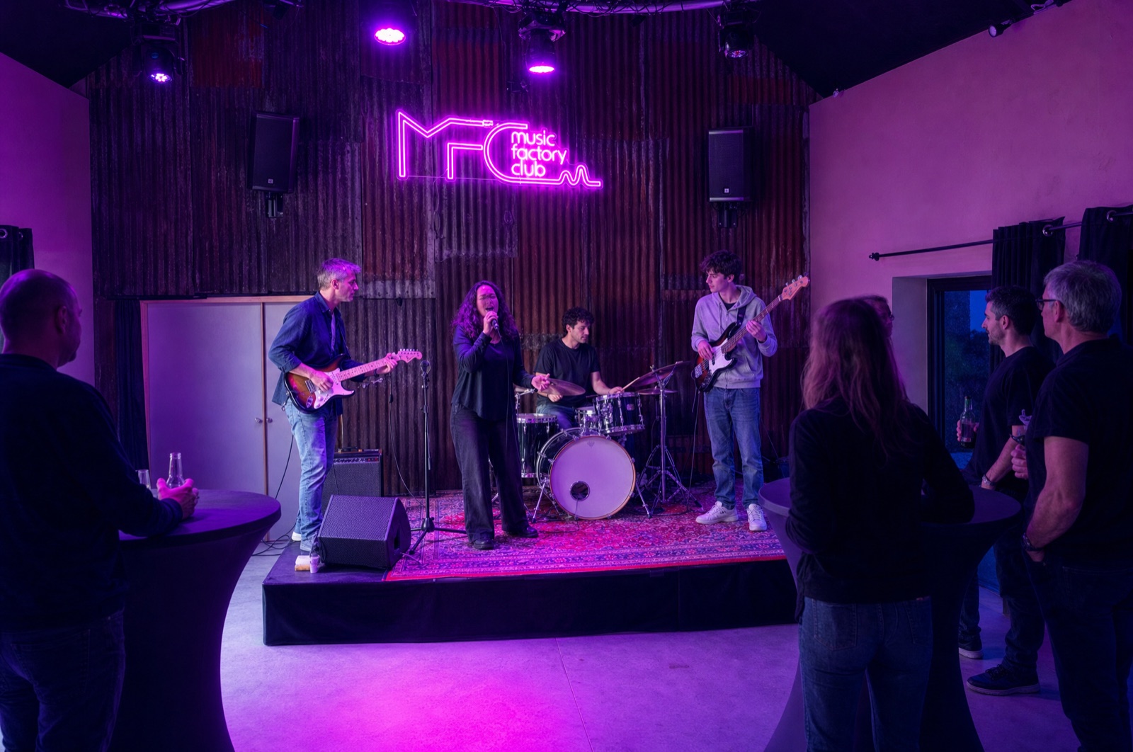 La scène du Music Factory Club pendant une jam : néon MFC, éclairage de concert, musiciens de tous âges